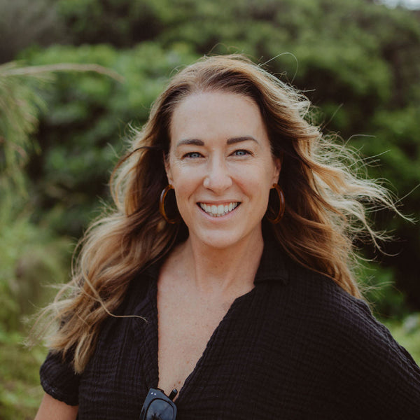 Woman with long hair smiling ath the beach outdoors with greenery in the background