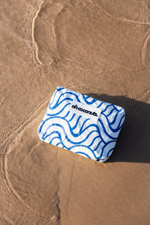 blue and white oh coconuts beach pouch laying in water at beach. 