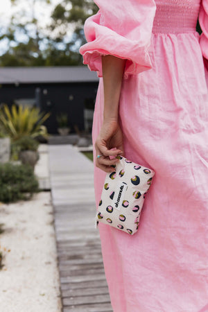 Person wearing a pink dress holding a small pouch with a leopard print design.