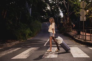 Model with polka dot beach bag on suitcase travelling to airport with luggage sleeve over suitcase. 