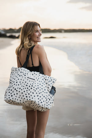 Model holding polka dot beach bag at sunset on beach with water bottle holder