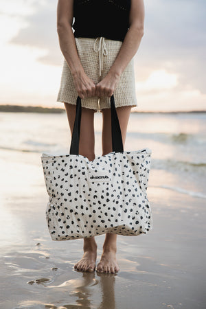 Model holding a polka dot beach bag on the beach with multiple pockets