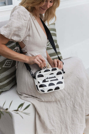 Woman holding a black and white patterned bag with 'oh coconut' branding on a light-colored couch.
