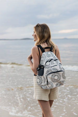 Model walking on beach with backpack with multiple pockets and waterbottle holder