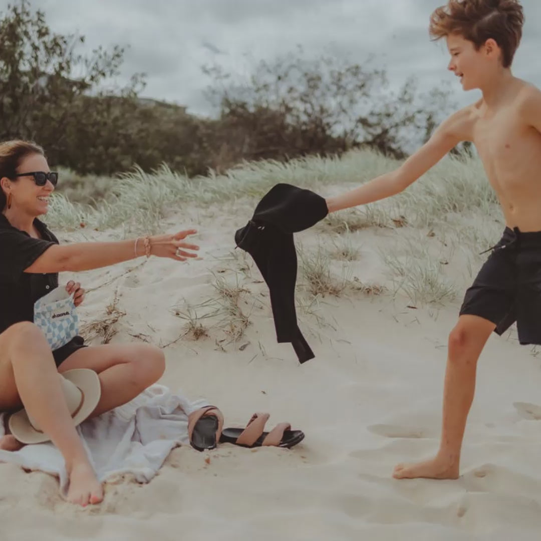 child handing mother wet rash guard to put in wet bag 